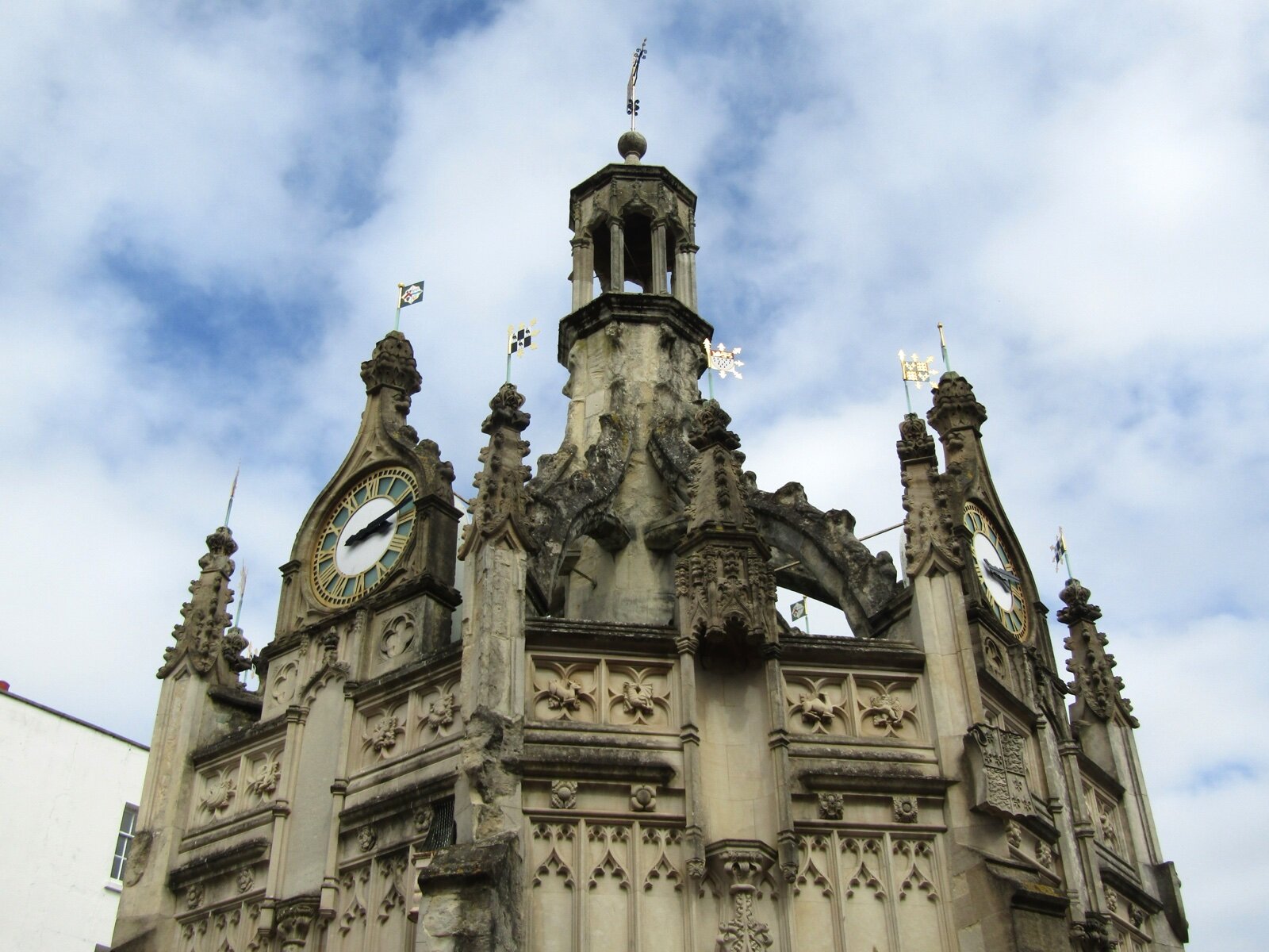The ornate stone Market Cross in Chichester city centre with clock faces and pinnacles against a cloudy sky