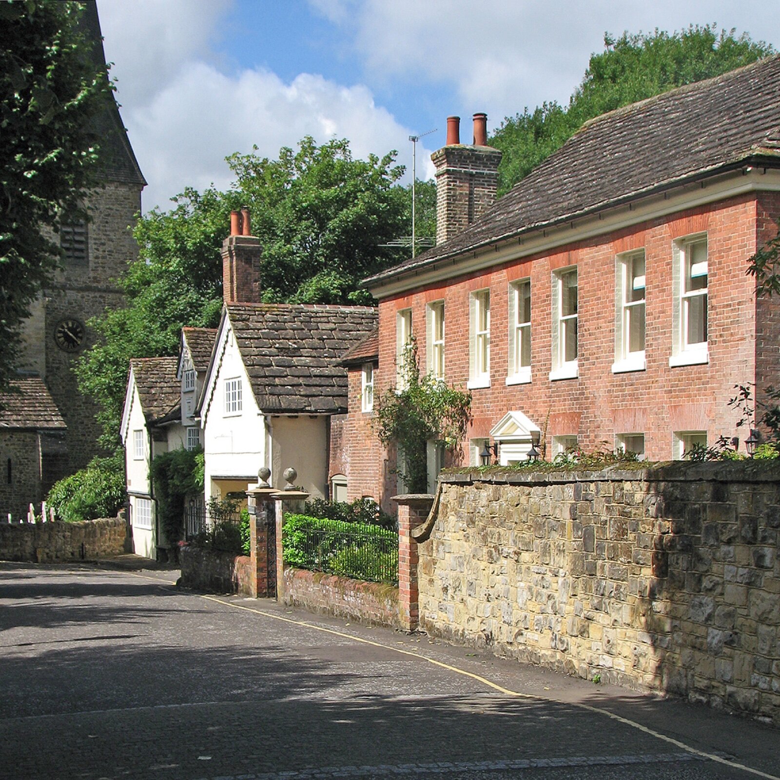 Listed brick and white-painted houses along the Causeway in Horsham, with the tower of St Mary's church behind trees on the left