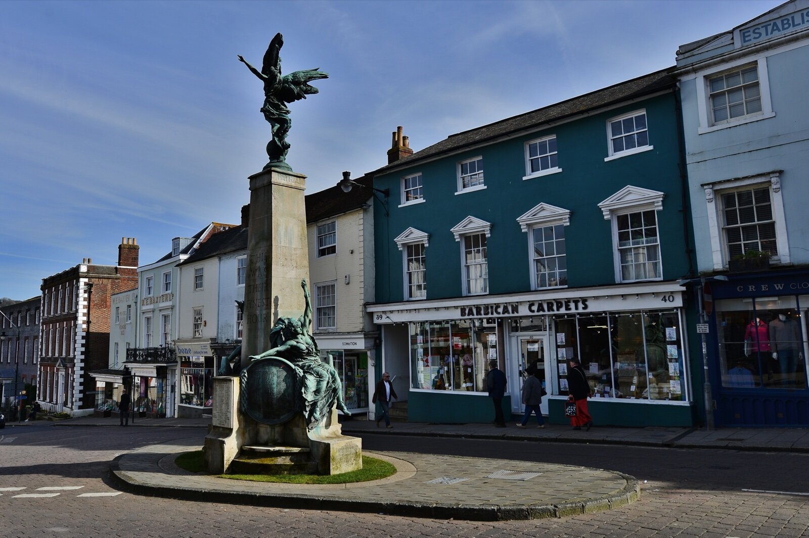 Lewes High Street with the bronze winged war memorial on a traffic island in front of a row of Georgian shopfronts