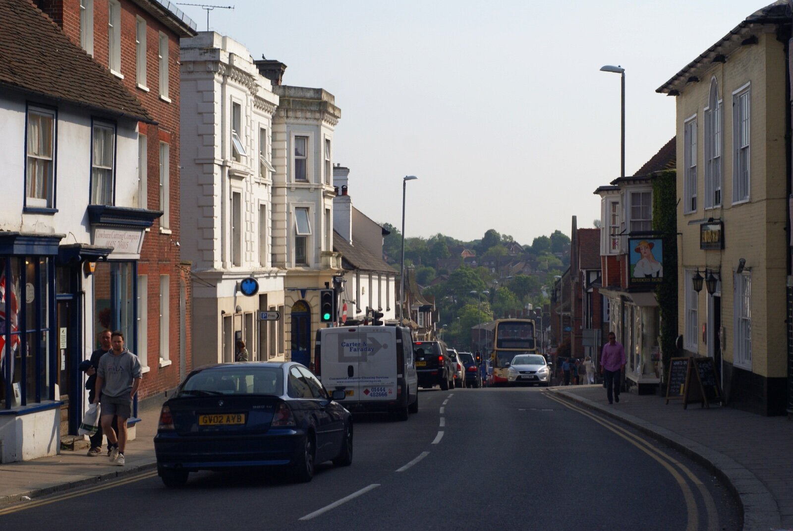 Uckfield High Street sloping downhill between older brick and painted buildings, with shops, cars and a bus