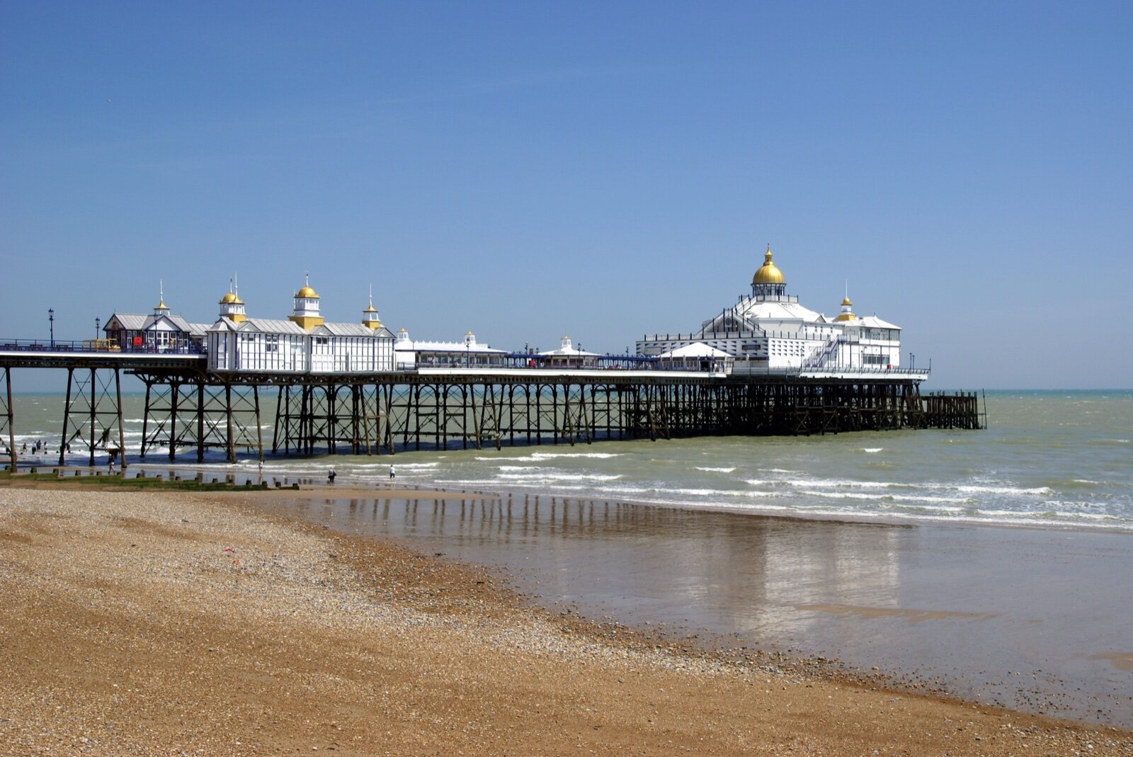 Eastbourne pier seen along the shingle beach on a clear day, with the seafront and the pier's gold domes