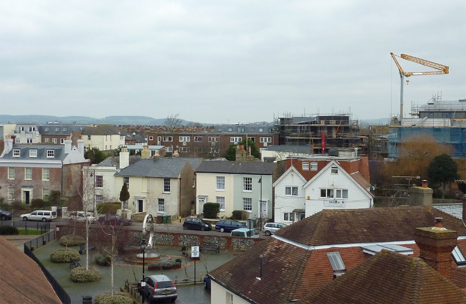 Rooftop view over terraced and detached houses on River Road in Littlehampton, with parked cars along the street and the South Downs on the horizon