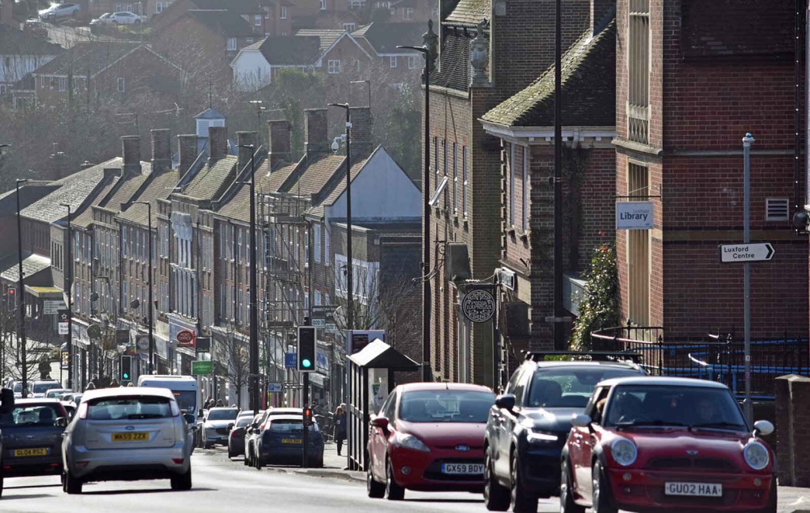 Uckfield High Street with traffic, terraced houses on the hill behind and a sign pointing to Luxford car park