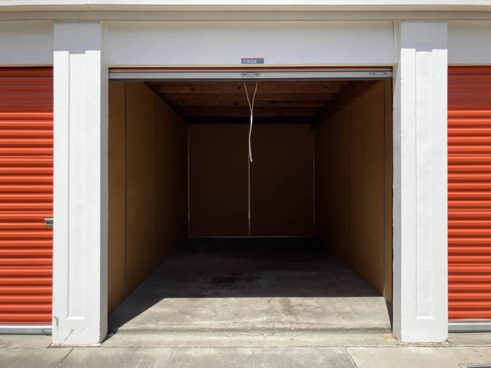 An open, empty self storage unit with the roller shutter raised and orange shutters on the units either side