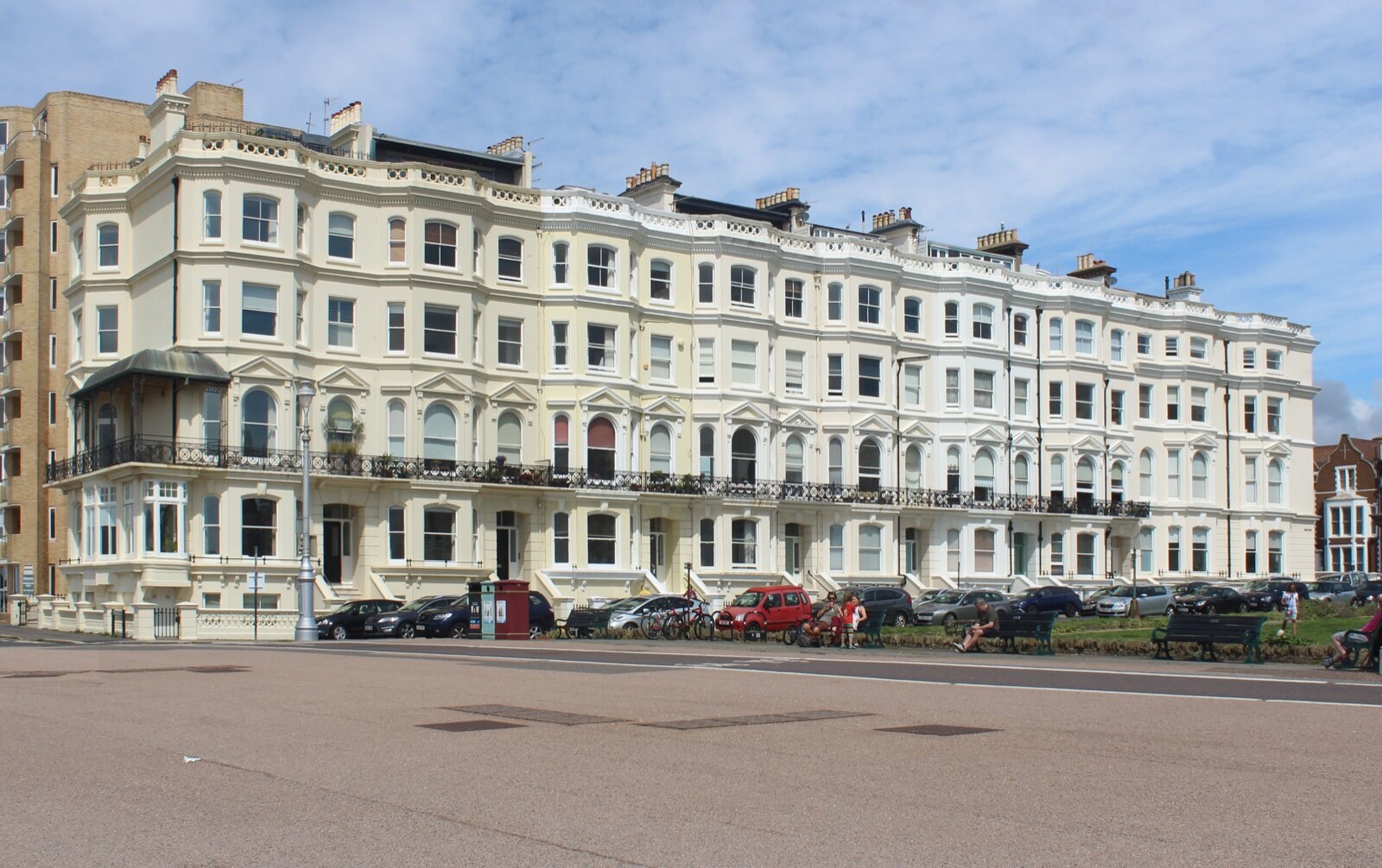 Medina Terrace in Hove, a long cream-painted Victorian seafront terrace of flats with bay windows and iron balconies, cars parked in front and people on benches