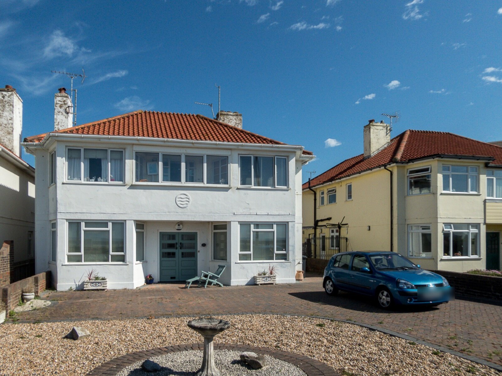 Two detached seafront houses with red tiled roofs on West Parade in West Worthing, one white and one cream, with a parked car and a gravel garden in front