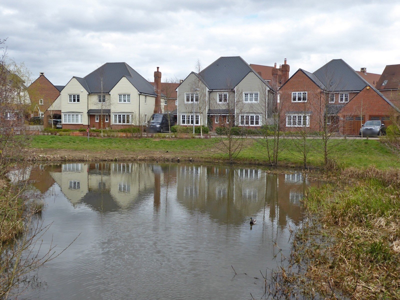 Modern detached and semi-detached houses behind a pond at Kilnwood Vale, near Faygate in Horsham district